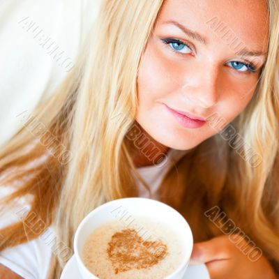 Smiling woman drinking a coffee lying on a bed at home or hotel.