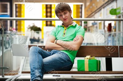 Portrait of young man inside shopping mall with gift box sitting