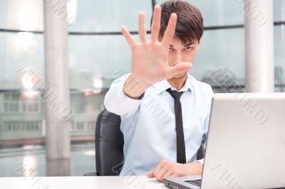 Angry young businessman sitting at his desk and showing stop ges