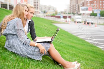 Portrait of two smiling women using laptop on a green meadow at 