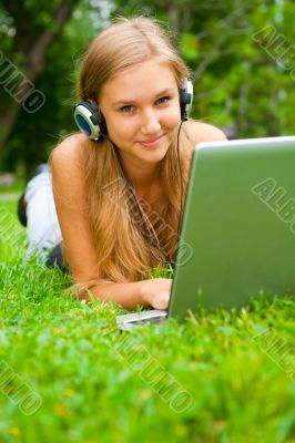 A smiling young girl with laptop outdoors listening music by hea