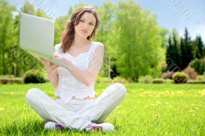 Young woman with laptop sitting on green grass