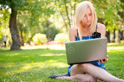 Beautiful student woman with a laptop sitting on green grass at 