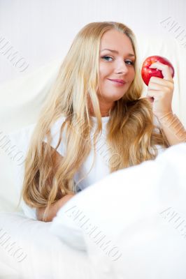 Young beautiful woman with apple in bed in the morning