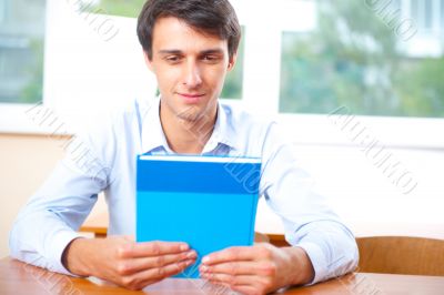 Portrait of a young handsome man with a book indoors