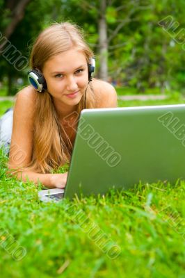 A smiling young girl with laptop outdoors listening music by hea