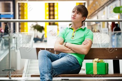 Portrait of young man inside shopping mall with gift box sitting
