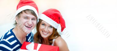 Young happy couple in Christmas hats standing together and holdi
