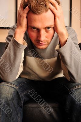 Closeup portrait of young man sitting on sofa with headache