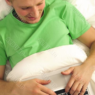Attractive man relaxing in bed. White silk linen. Working by is 