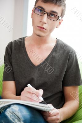 Young adult man writing in his copybook while sitting on a large