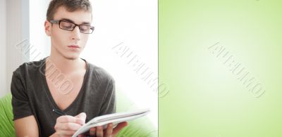 Young adult man writing in his copybook while sitting on a large