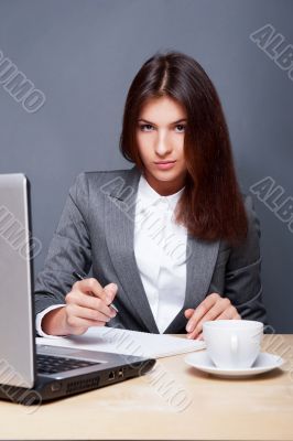 A pretty concentrated woman working with her laptop and papers. 