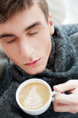 Portrait of a young man drinking coffee while sitting on armchai