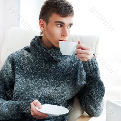 Portrait of a young man drinking coffee while sitting on armchai
