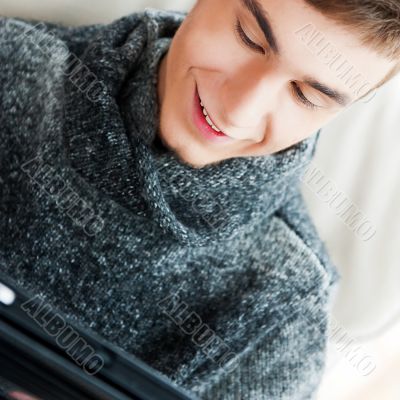 Happy young handsome man at home, smiling and using his tablet c