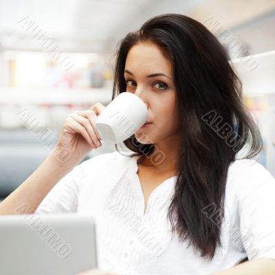 Portrait of a beautiful young woman working on laptop and drinki