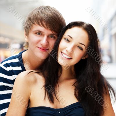 Portrait of young couple embracing at shopping mall and looking 