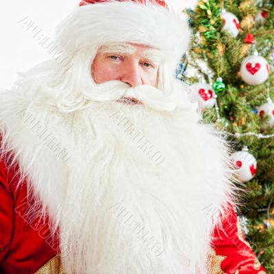 Santa sitting at the Christmas tree, fireplace and looking at ca