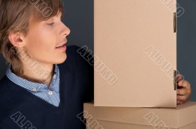 Portrait of young man leaning on box against grey wall. He is st