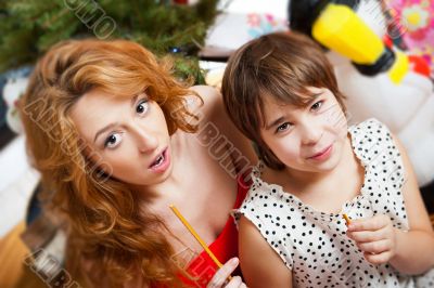 Mother and her daughter sitting together near christmas tree. To