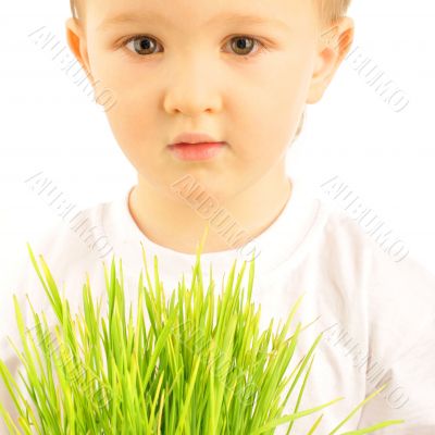 Happy little boy holding green grass in his arms and looking ser