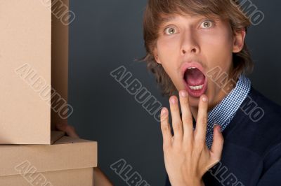 Portrait of young man with boxes against grey wall. He is afraid