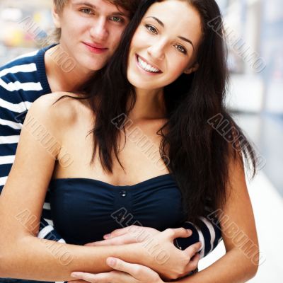 Portrait of young couple embracing at shopping mall and looking 
