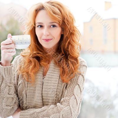 Portrait of beautiful red hair girl drinking coffee on winter ba