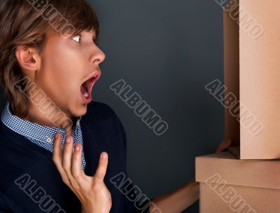 Portrait of young man with boxes against grey wall. He is afraid