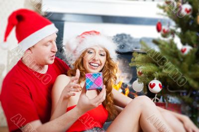 Young happy couple near a Christmas tree at home holding gift an
