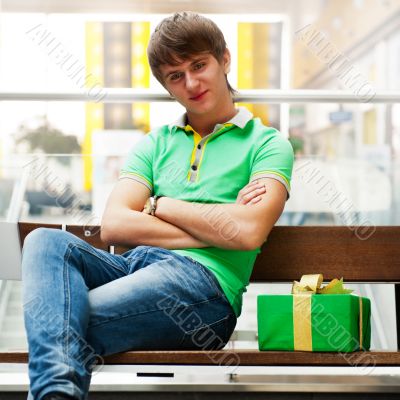 Portrait of young man inside shopping mall with gift box sitting