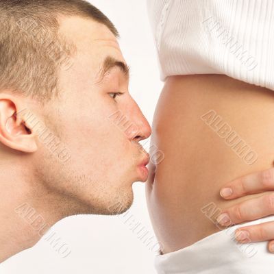 Man kissing his wife`s belly at home against wall