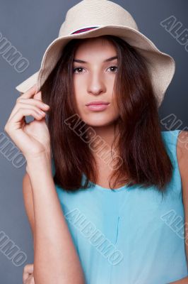 Confident woman with arms near her head holding hat against a bl