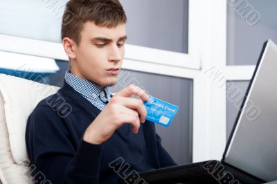Handsome man holding credit card and using laptop for online sho Handsome man holding credit card and using laptop for online sho