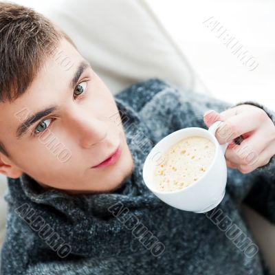 Portrait of a young man drinking coffee while sitting on armchai Portrait of a young man drinking coffee while sitting on armchai