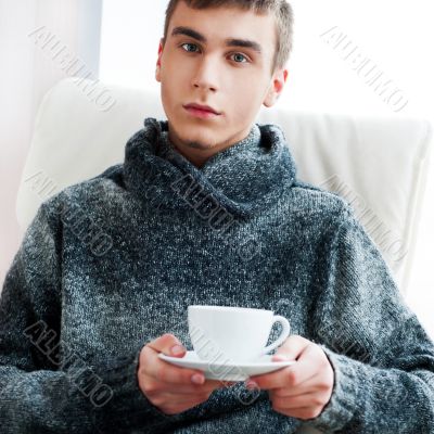 Portrait of a young man drinking coffee while sitting on armchai Portrait of a young man drinking coffee while sitting on armchai