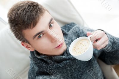 Portrait of a young man drinking coffee while sitting on armchai Portrait of a young man drinking coffee while sitting on armchai