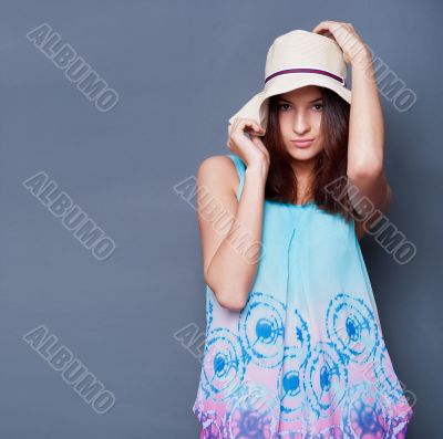 Confident woman with arms near her head holding hat against a bl