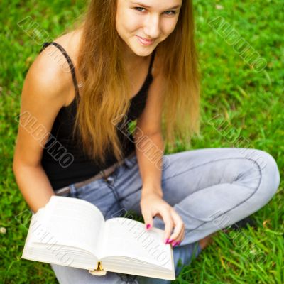 Beautiful female student outdoors with a book at campus park