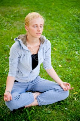 Portrait of young woman meditating in pose of lotus on green gra