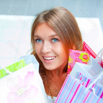 Shopping woman with lots of bags smiles inside mall. She is happ