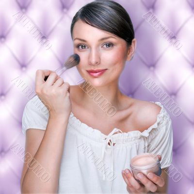 Portrait of attractive young adult woman applying blusher agains