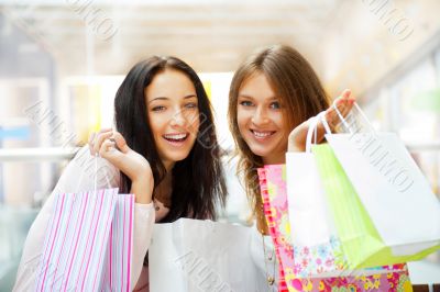 Two excited shopping woman together inside shopping mall. Horizo