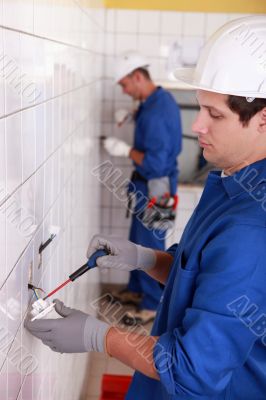 Pair of electricians wiring a white tiled room