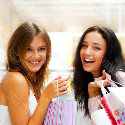 Two excited shopping woman together inside shopping mall. Horizo