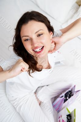 Portrait of young beautiful awake woman with gifts on bed at bed