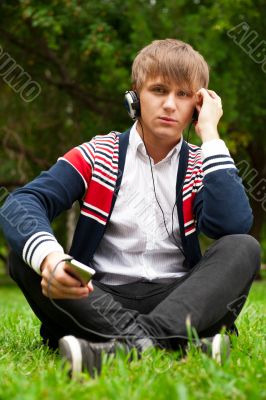 Student outside sitting on green grass and listening music via h