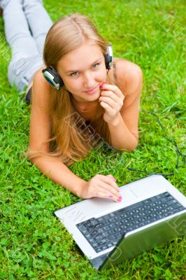 A smiling young girl with laptop outdoors listening music by hea