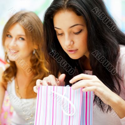 Two excited shopping woman resting on bench at shopping mall. Lo